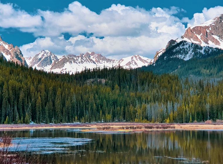 Snow capped Colorado peaks above an alpine lake and pine forest